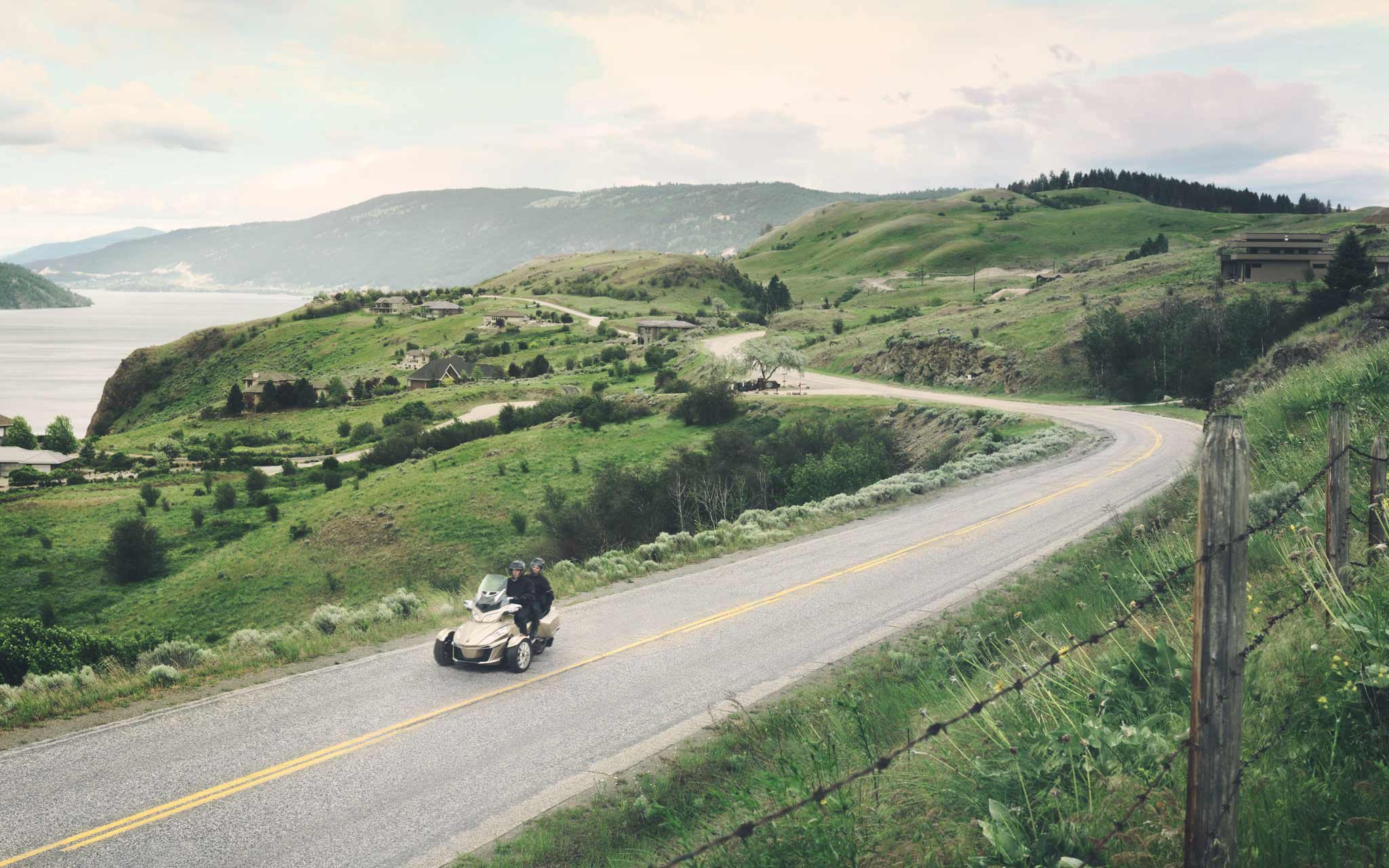 wide elevated shot looking down road twisting through green hills while Can Am Spyder rides by