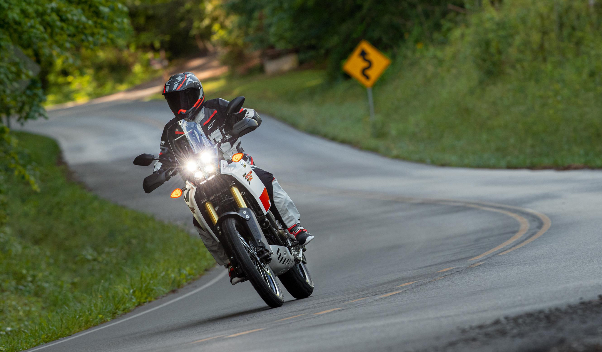 Rider on Yamaha Tenere 700 taking twisty turns through woody road