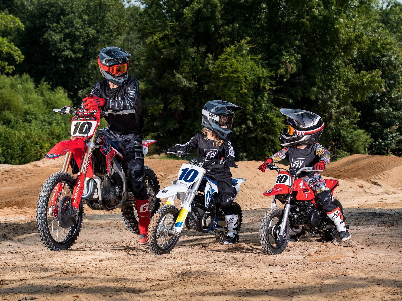 Two kids and adult pose on dirt bikes at track